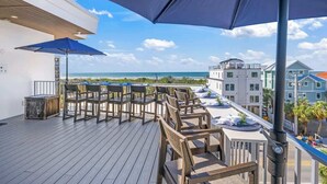 A deck with wooden chairs and tables, umbrellas, and a view of the ocean and buildings. - Steps to Beach/Gulf Views/Pool Volleyball/Slide (Siesta Key)