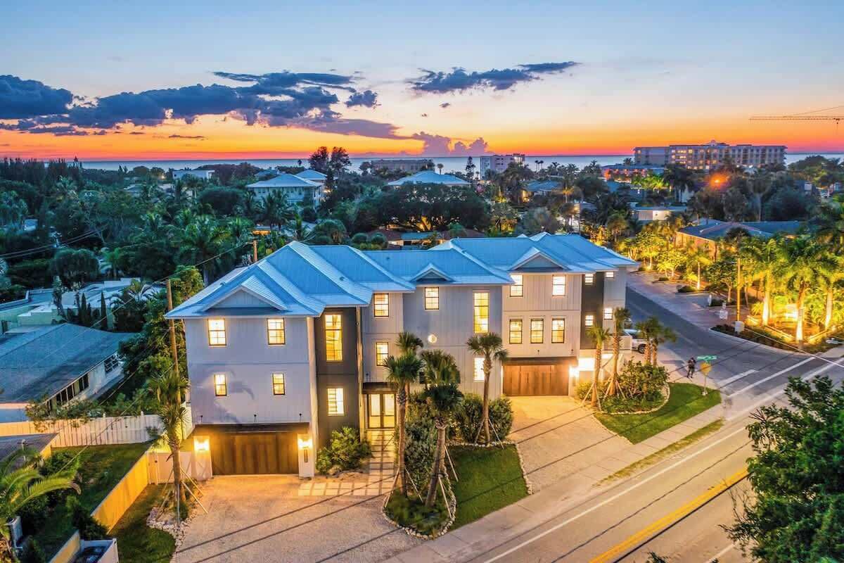 A modern two-story house with a garage, surrounded by a well-maintained lawn and palm trees, set against a sunset backdrop.