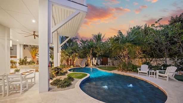 A modern outdoor pool area with a curved design, surrounded by lush greenery and palm trees. - Steps to Beach/Pool w/Slide and Chipping Green (Sarasota)