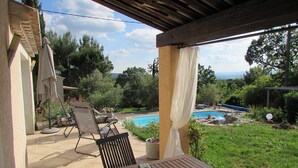 Une terrasse extérieure avec une table et des chaises en bois, une piscine et une vue sur le paysage environnant.