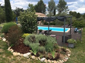 Un jardín ajardinado con piscina, mobiliario exterior y un pérgola.