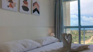 Habitación de hotel con una cama grande, almohadas blancas y vistas a un paisaje a través de un ventanal.