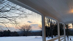 Ein überdachter Balkon mit Blick auf eine verschneite Landschaft und kahle Bäume.