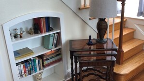 Eine Treppe mit hölzernen Geländern und einer weißen Wand.  Dazu gehören ein kleiner Tisch, eine Lampe und ein Bücherregal voller Bücher.