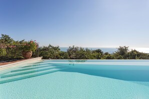 A clear blue infinity pool with a view of the ocean and lush greenery. - Villa Vanisia (acicastello)