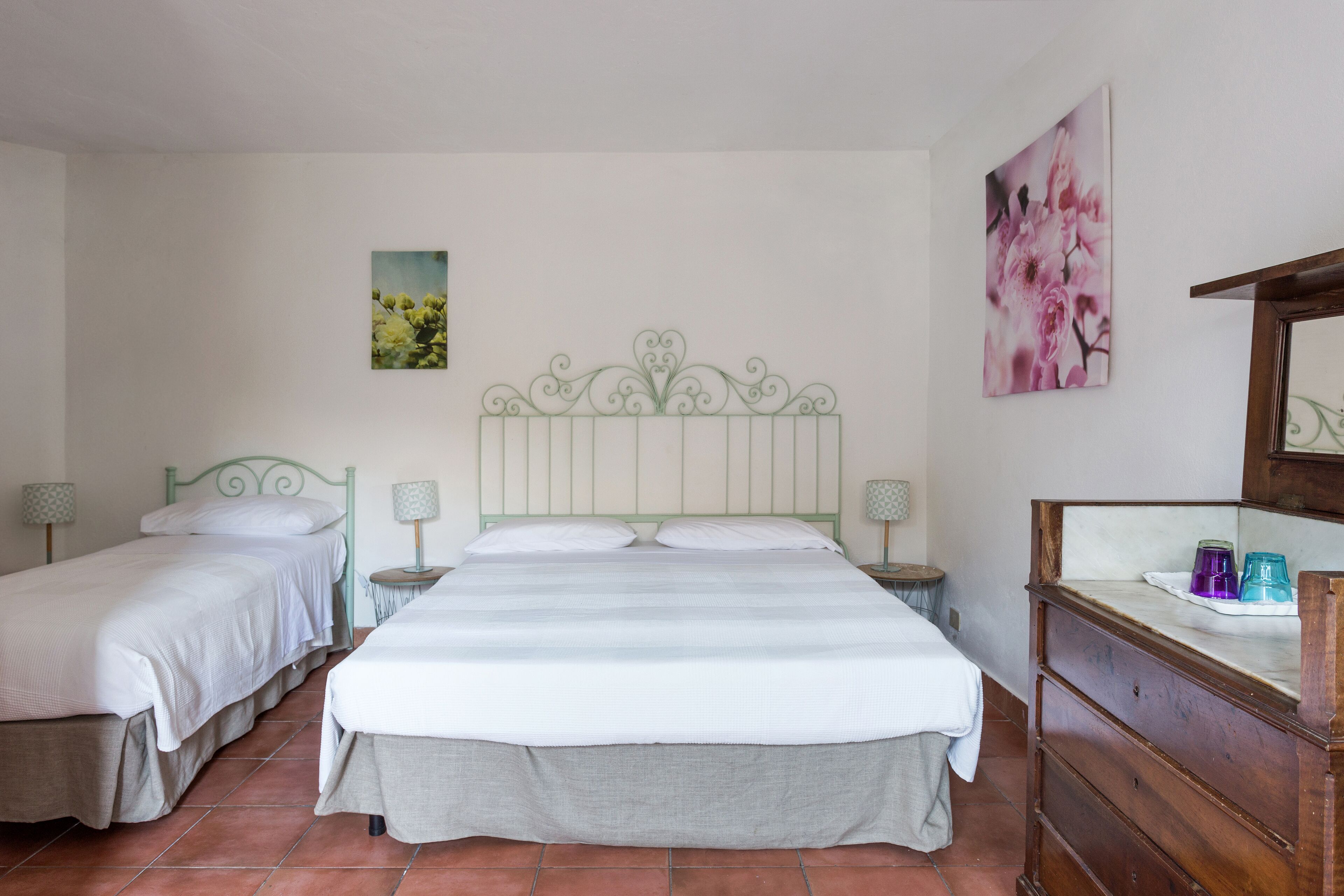A bedroom with two single beds, a large bed, a dresser, and two bedside tables with lamps.