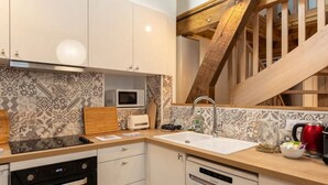Eine moderne Küche mit weißen Schränken, einer Mikrowelle, einem Spülbecken und einer Holztreppe.