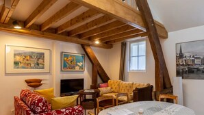 Ein gemütliches Wohnzimmer mit hohen Holzbalken, einem Kamin, einer Sofagarnitur und gerahmten Bildern an den Wänden.