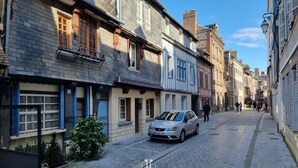 Eine gepflasterte Straße gesäumt von historischen Gebäuden, ein geparktes Auto und einige Fußgänger.