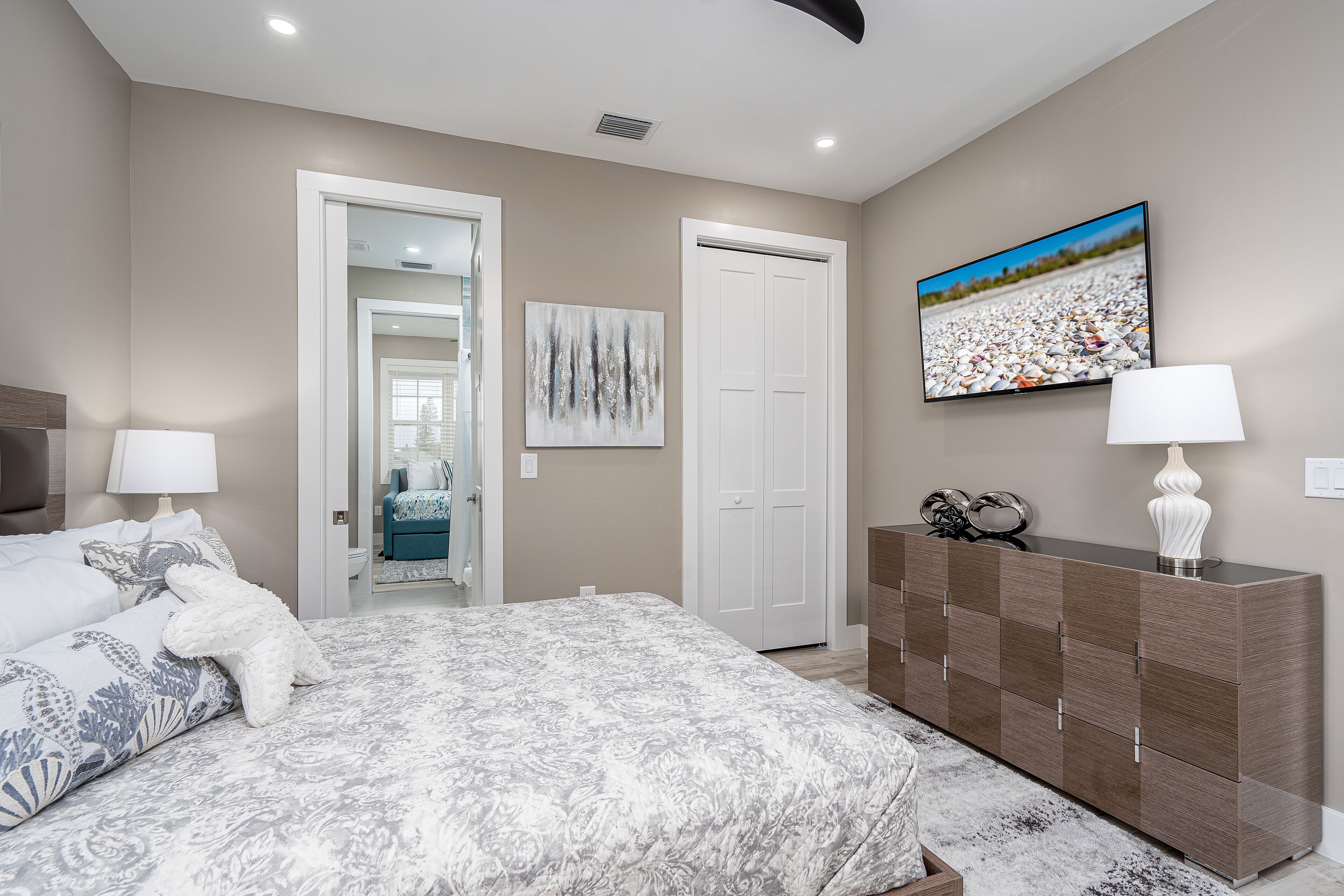 Une chambre à coucher comprenant un lit, des lampes de chevet, une commode, un tableau et une porte donnant sur une autre pièce.