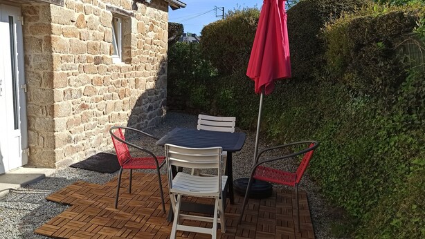 A stone building with a door, a table with chairs, and a red umbrella.