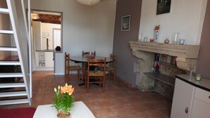 A dining area with a table, chairs, a potted plant, a fireplace, and a kitchen in the background.