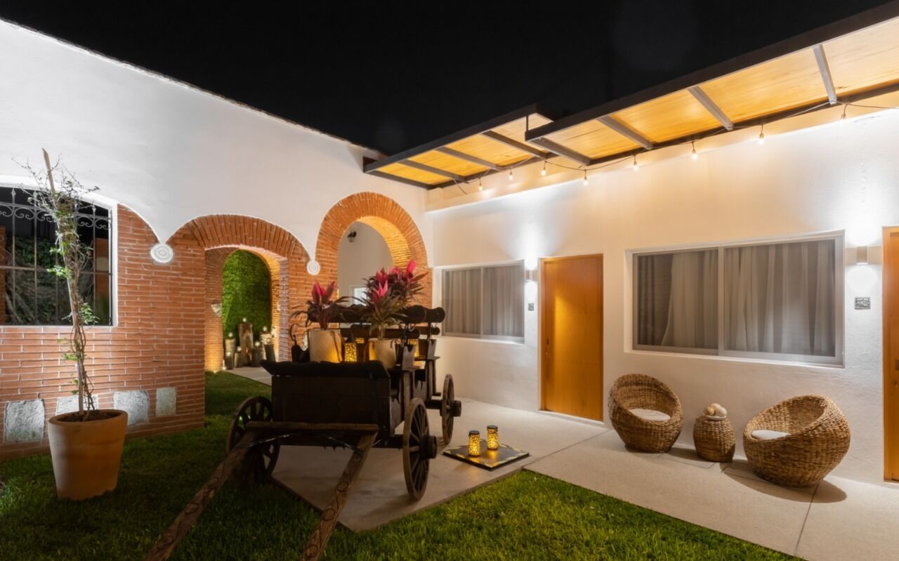 Un espacio exterior moderno con un muro de ladrillo, un carrito de madera, sillas de mimbre y una entrada bien iluminada.