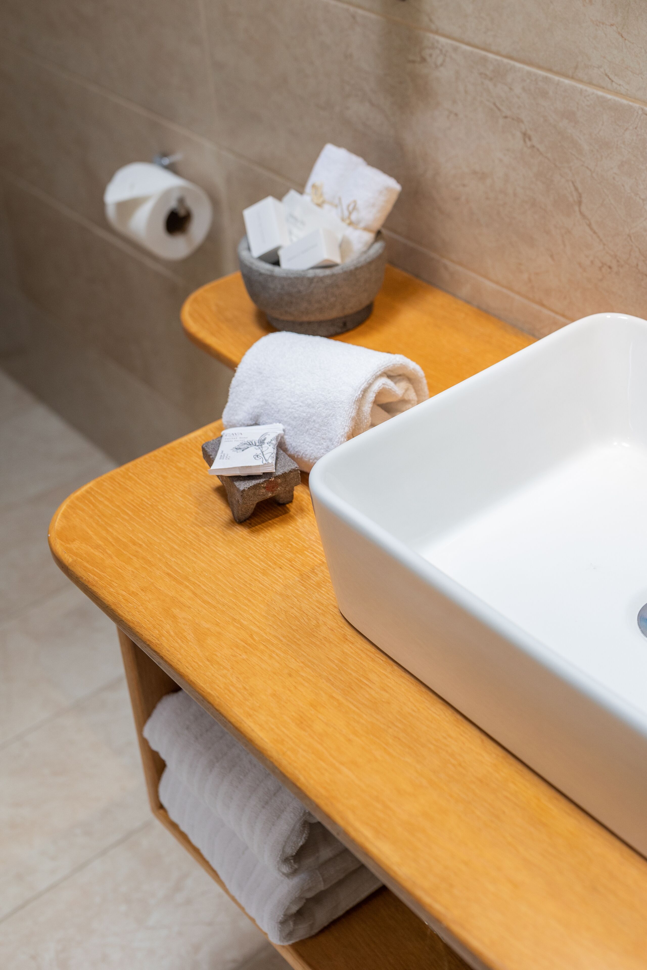 A bathroom with a wooden vanity, a white sink, and a bowl containing toiletries.