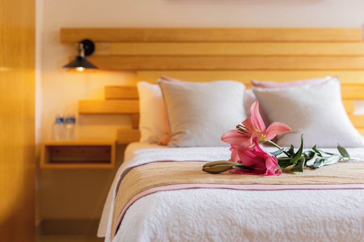 A hotel room with a neatly made bed, a bedside table with a lamp, and a bouquet of flowers on the bed.