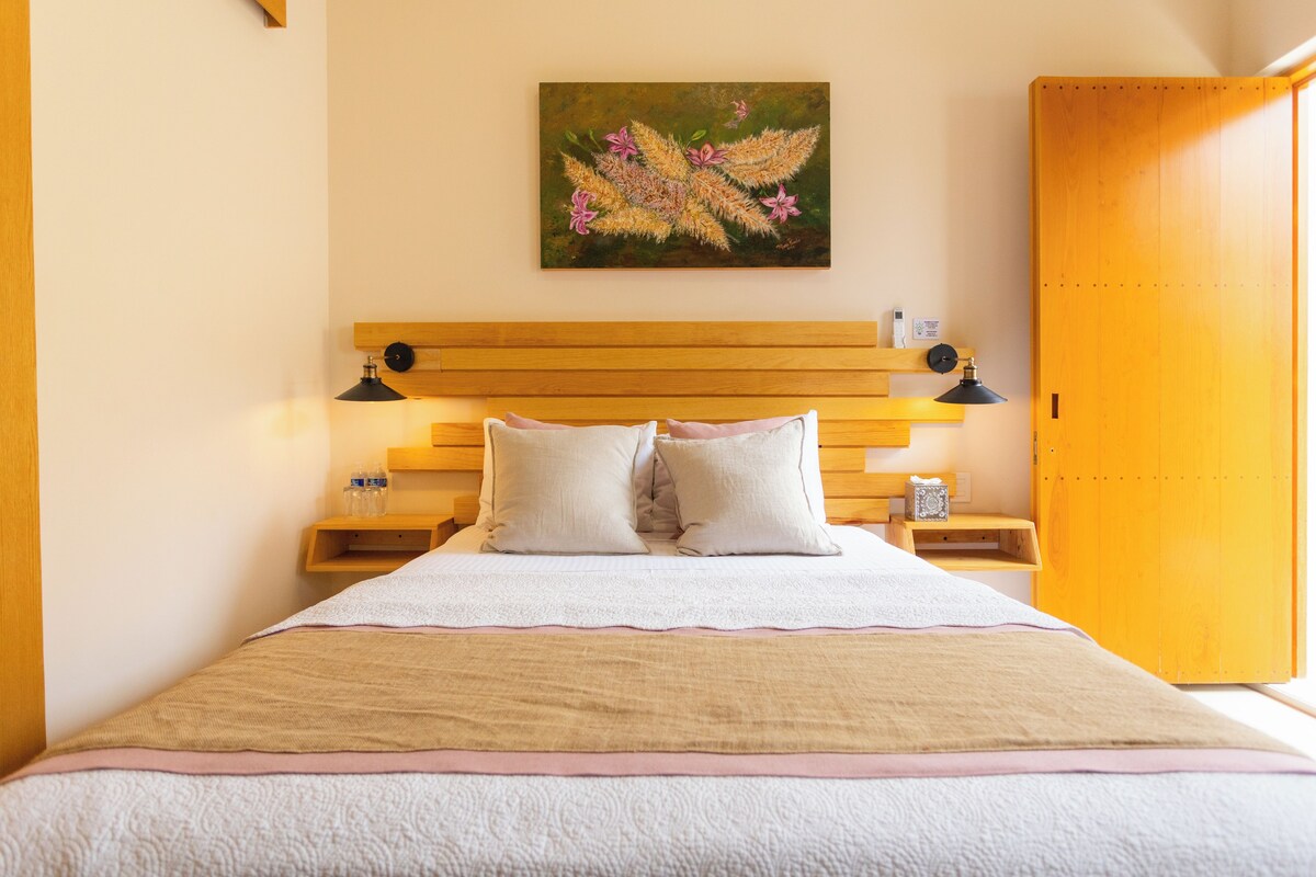 A neatly made bed with a wooden headboard, two bedside tables with lamps, and a painting on the wall.