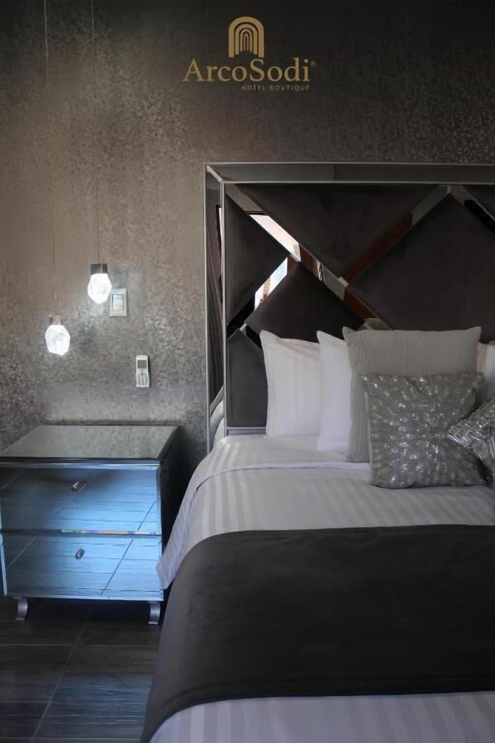 A modern hotel room with a bed, bedside tables, and wall-mounted lights.