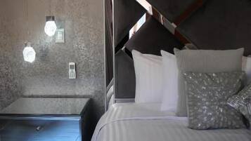 A modern hotel room with a bed, bedside tables, and wall-mounted lights.