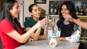 Three people toasting with glasses at a table with bottles and a candle. - ArcoSodi Hotel Boutique (Oaxaca)
