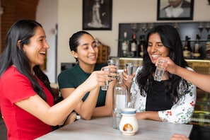 Three people toasting with glasses at a table with bottles and a candle. - ArcoSodi Hotel Boutique (Oaxaca)