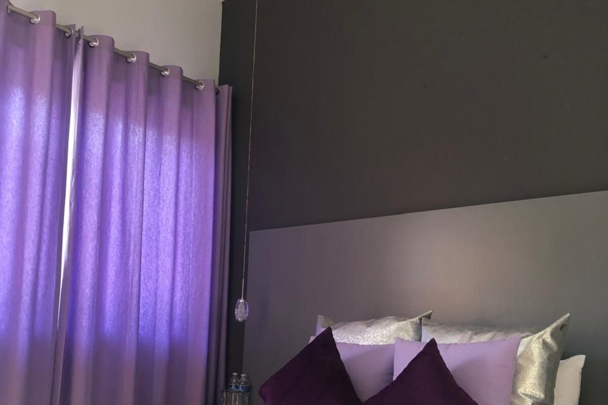 A modern bedroom with a large bed, purple bedding, and a dark accent wall.