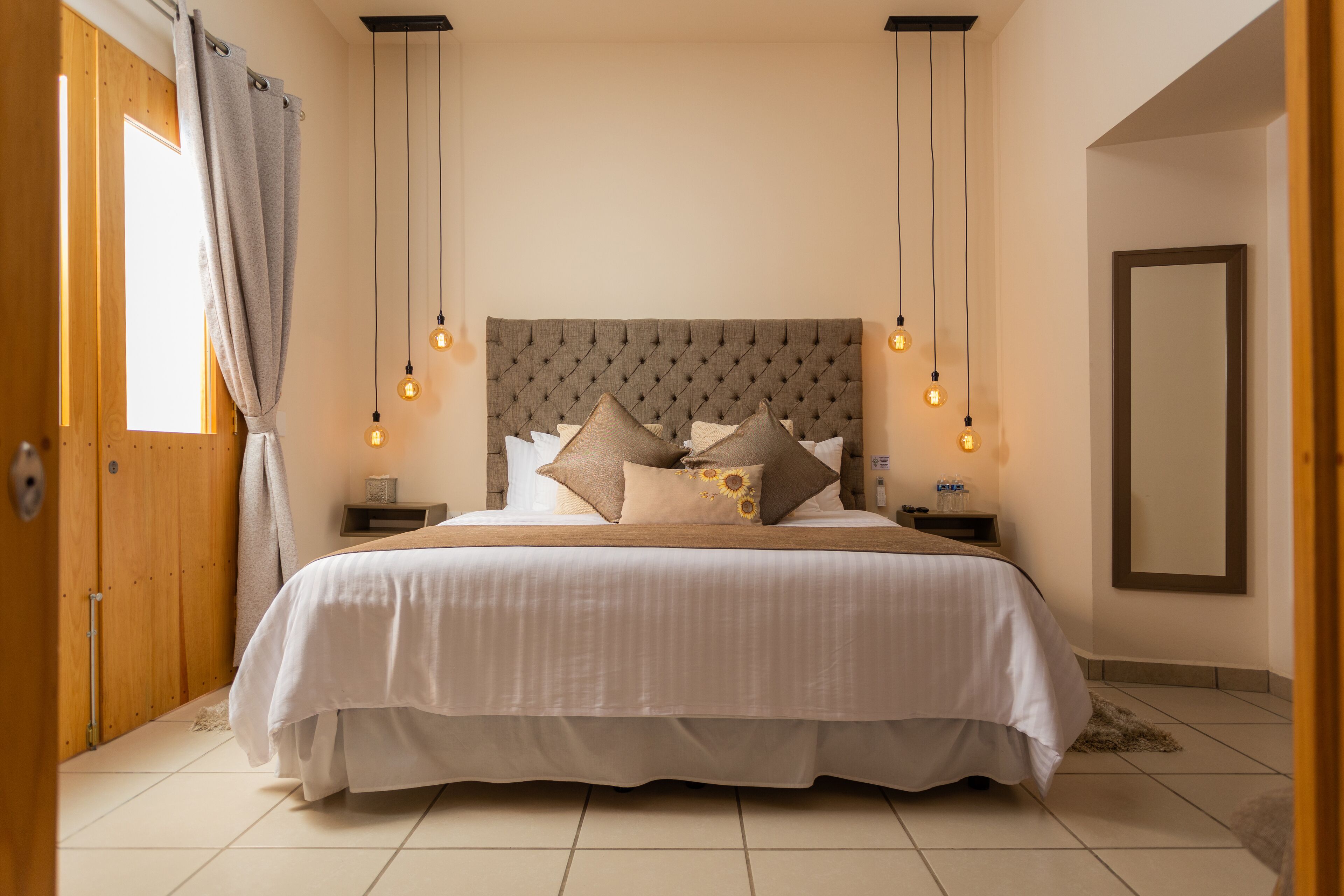 A bedroom with a large bed, a wooden headboard, bedside tables, and a mirror on the wall.