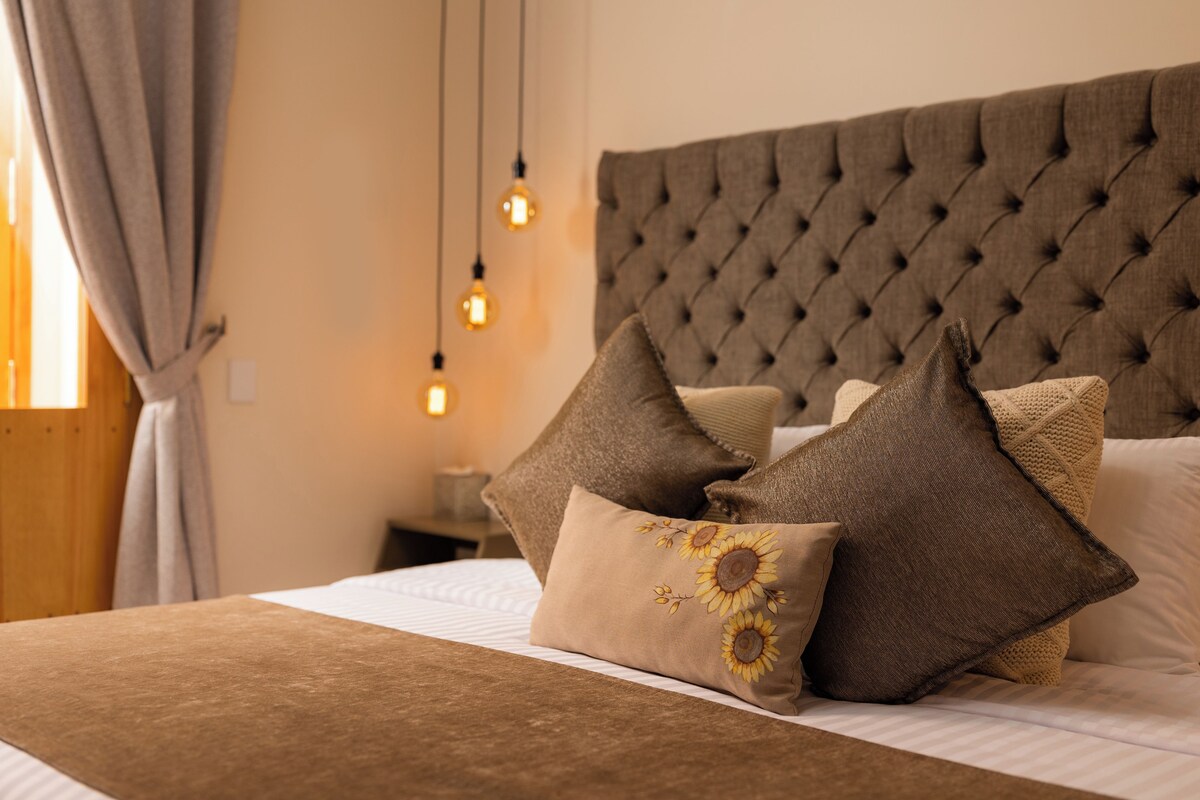 A neatly made bed with a tufted headboard, multiple pillows, and a brown throw blanket.