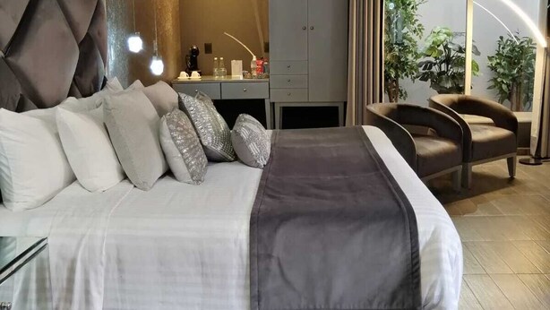 A modern bedroom with a large bed, a desk, and a chair. There is a wardrobe and a view of greenery outside. - ArcoSodi Hotel Boutique (Oaxaca)