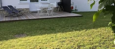 Un patio con mobiliario exterior, un edificio blanco con techo de tejas y un césped.