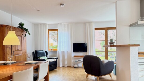 A modern living room with a dining area, a flat-screen TV, and a balcony with a view.