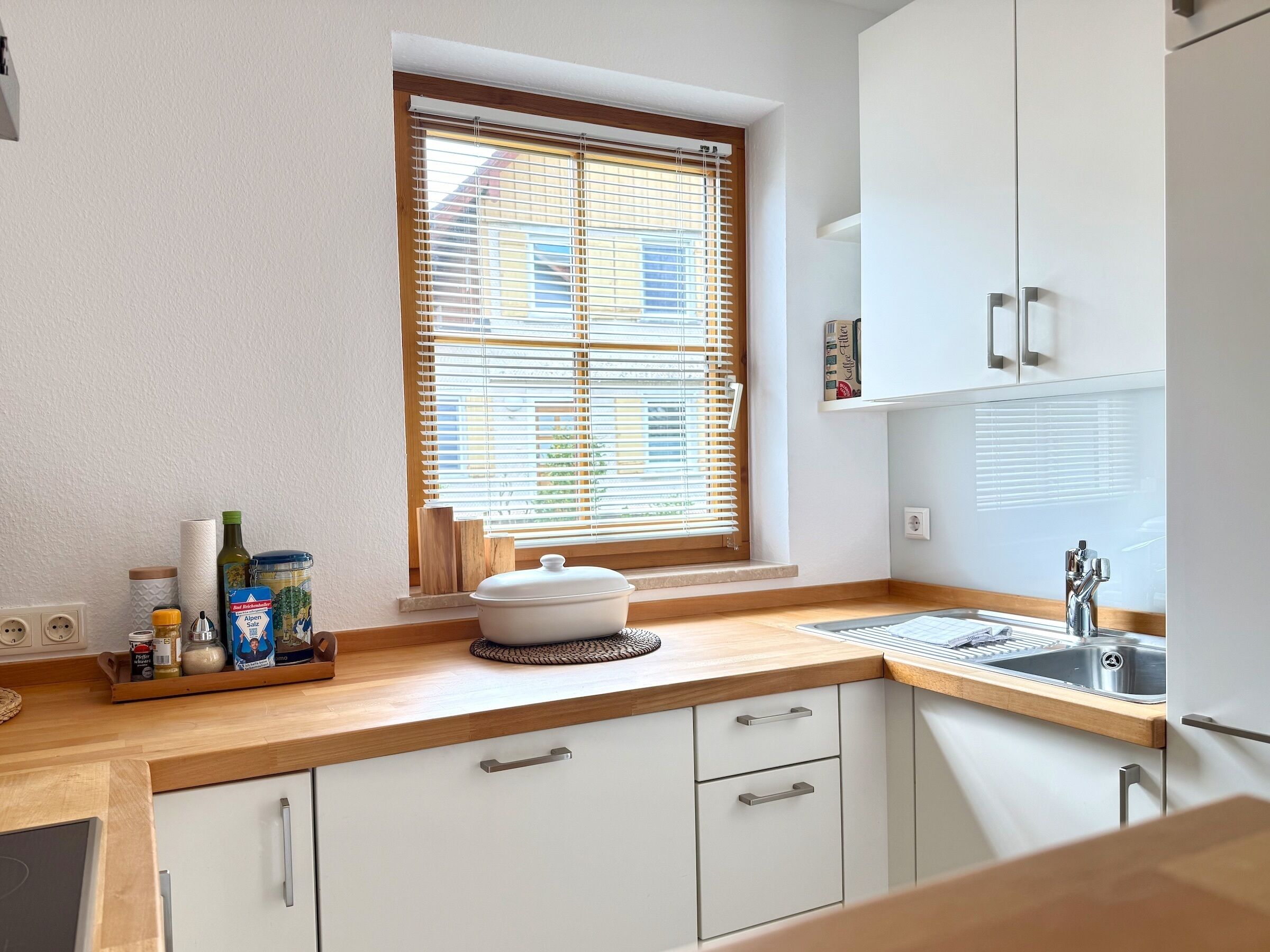 A kitchen with a window, wooden countertop, white cabinets, and a sink.