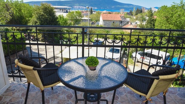 Ein Balkon mit zwei Korbstühlen und einem Glastisch, mit Blick auf eine Stadt, Gebäude und einen Berg in der Ferne.