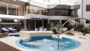 Ein moderner Poolbereich im Freien mit Liegestühlen, einem Whirlpool und Blumentöpfen.