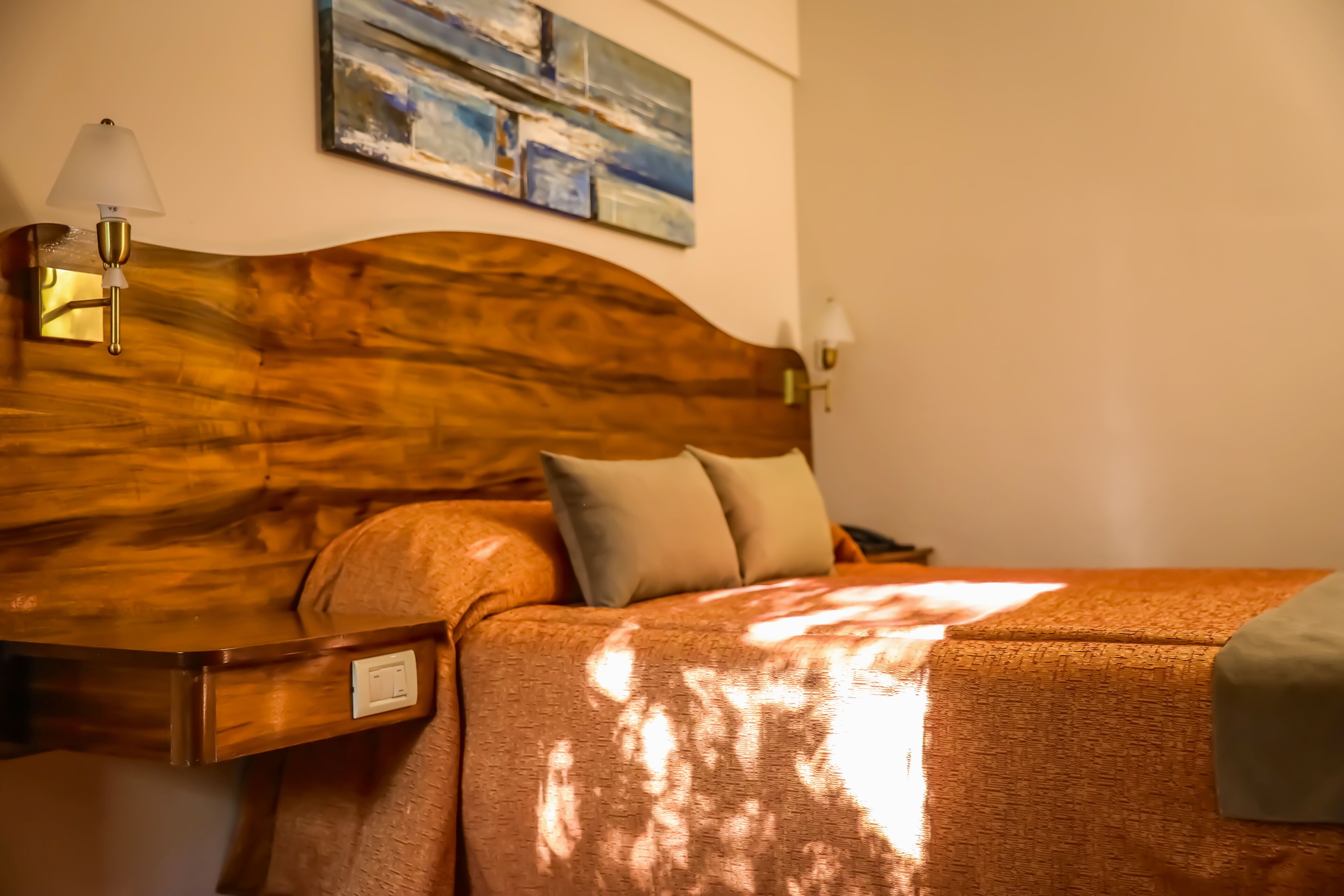 A neatly made bed with a wooden headboard, a bedside table with a lamp, and a painting on the wall.
