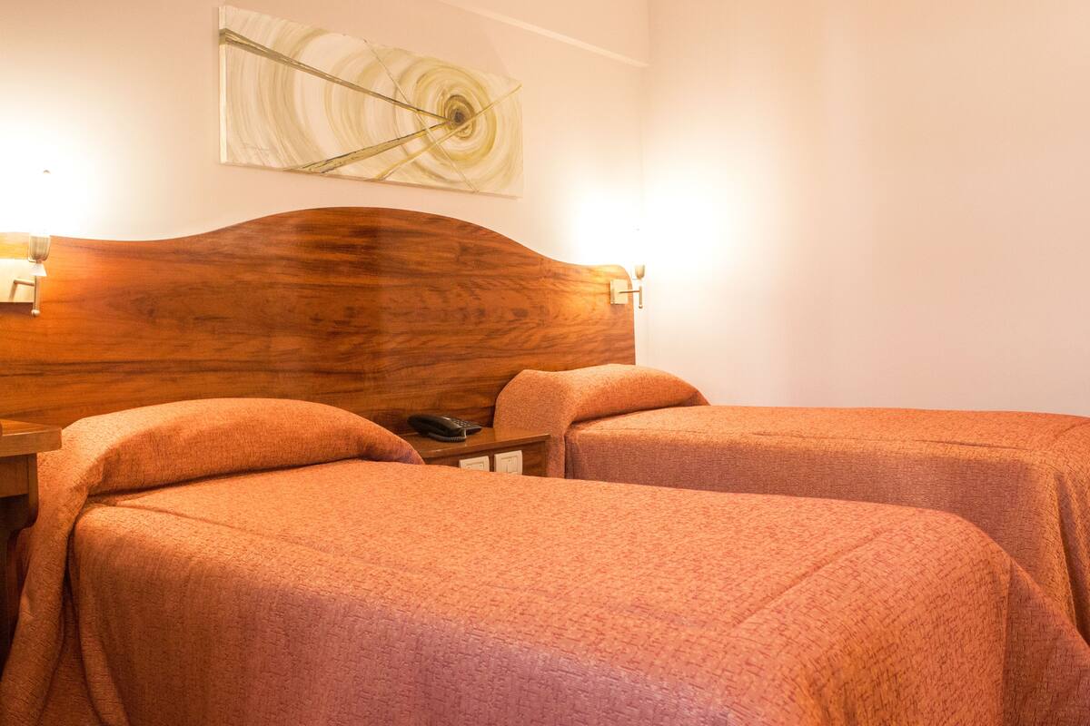 A hotel room with two beds, a wooden headboard, a nightstand, and a wall-mounted artwork.