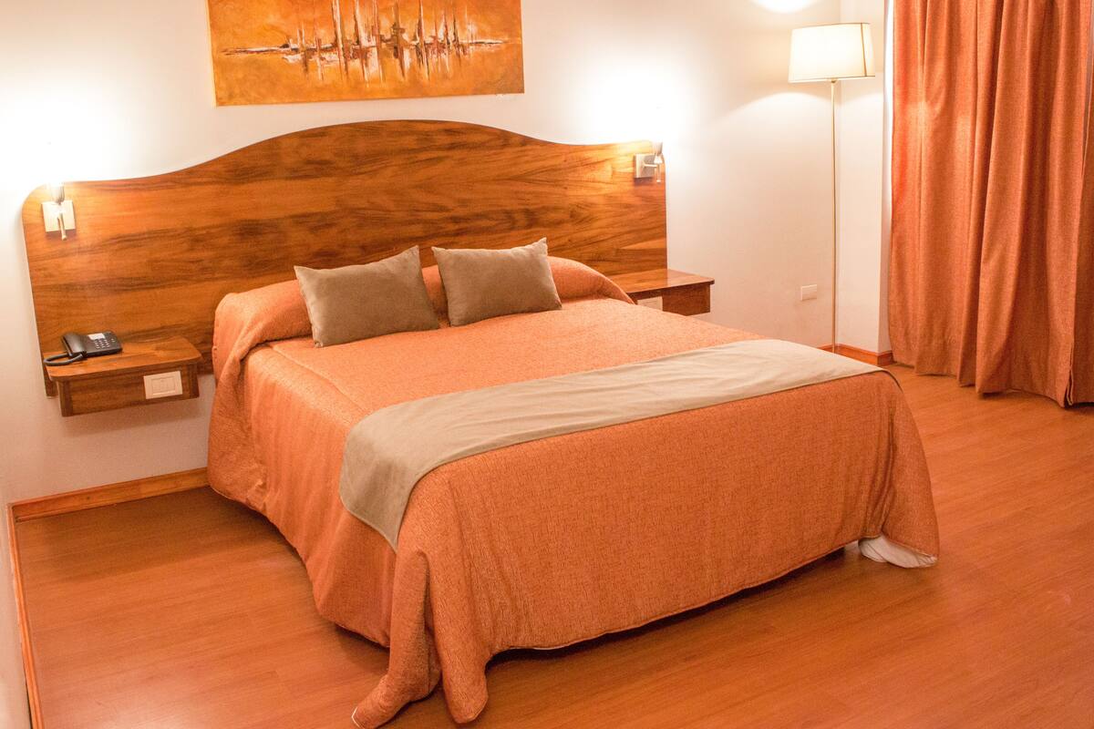 A neatly made bed with a wooden headboard, a bedside table with a lamp, and a painting on the wall.