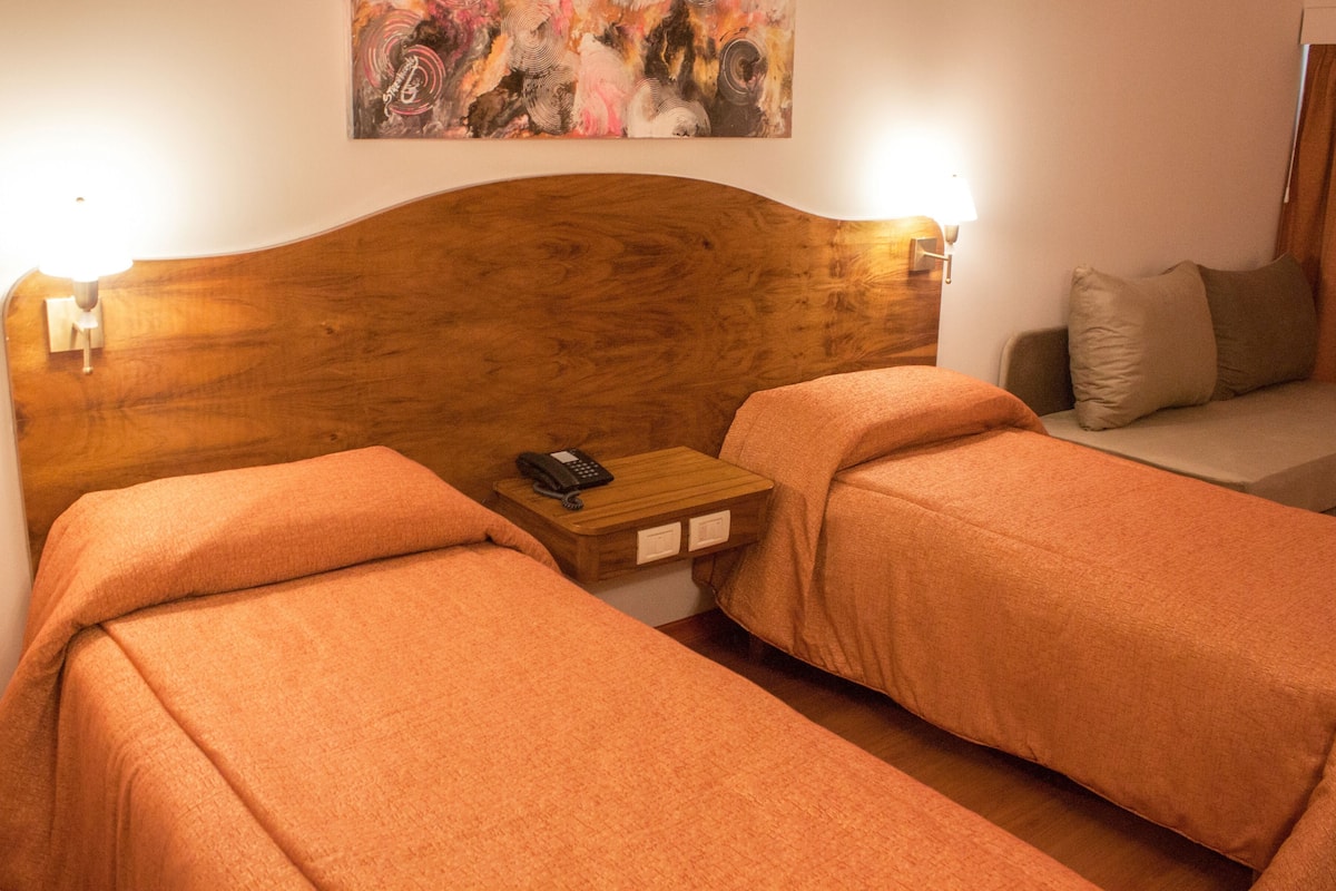 A hotel room with two beds, a wooden headboard, a bedside table with a phone, and a painting on the wall.
