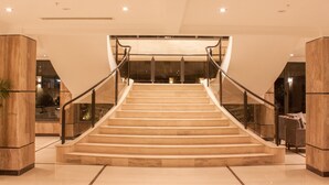 Eine imposante Treppe mit Marmorstufen und Glasgeländern, gesäumt von hohen Holzsäulen und Blumentöpfen.