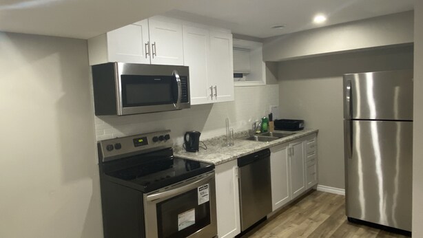 A modern kitchen with stainless steel appliances, white cabinetry, and a granite countertop.