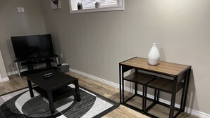 A living room with a TV, a black coffee table, a wooden side table with a vase, and a patterned rug.