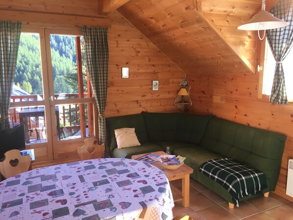 A cozy cabin with a green sofa, a wooden table with a basket, and a bed with a patterned bedspread.