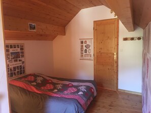 A bedroom with a wooden ceiling, a bed with a patterned blanket, a door, and two posters on the wall.
