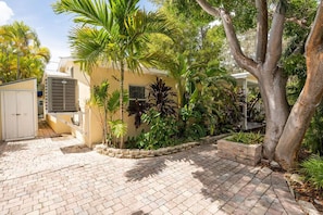 A paved driveway leading to a house with a large tree and various plants. - BE STILL- 4 Bedroom, 3 Bath with POOL & Guest Cottage (Key West)