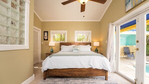 A bedroom with a bed, two windows, a ceiling fan, and a view of a pool outside. - BE STILL- 4 Bedroom, 3 Bath with POOL & Guest Cottage (Key West)