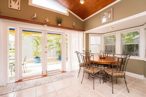 A dining area with a wooden table and metal chairs, a large window with blinds, and a view of the outdoors. - BE STILL- 4 Bedroom, 3 Bath with POOL & Guest Cottage (Key West)
