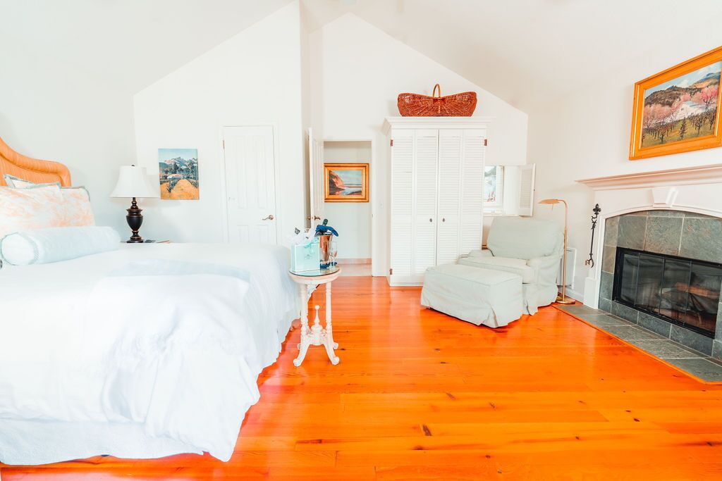A bedroom with a bed, a dresser, a chair, a fireplace, and a hallway.
