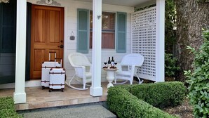 A house with a porch, a wooden door, and two rocking chairs. There are two suitcases and a table with bottles on the porch. - Private Napa Valley Cottage, Peaceful, Pet Friendly, and Walkable to Downtown (Calistoga)
