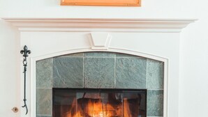A fireplace with a stone surround, a framed painting above it, and a wooden floor.