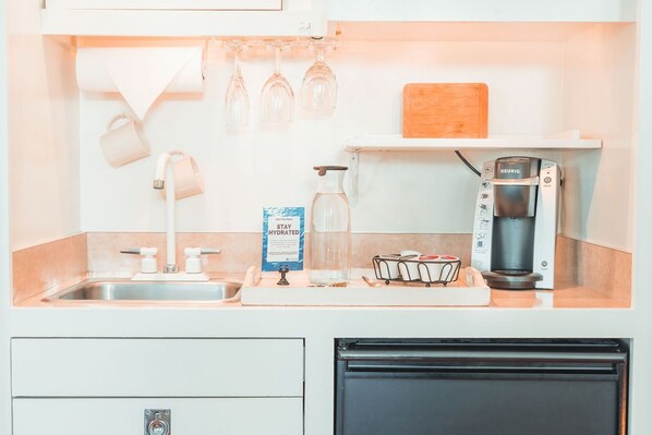 Una cocina con cafetera, jarra de agua y tabla de cortar sobre la encimera.