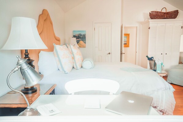 A bedroom with a bed, a desk with a laptop, a lamp, and a wardrobe.